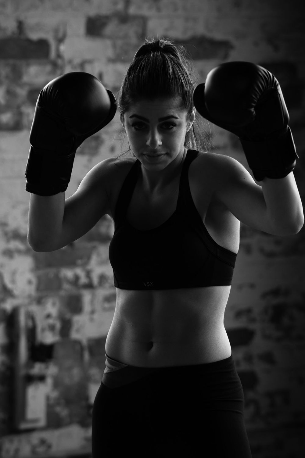 Dramatically lit b&w portrait of a female Thai boxer in a black tank top 16oz boxing gloves