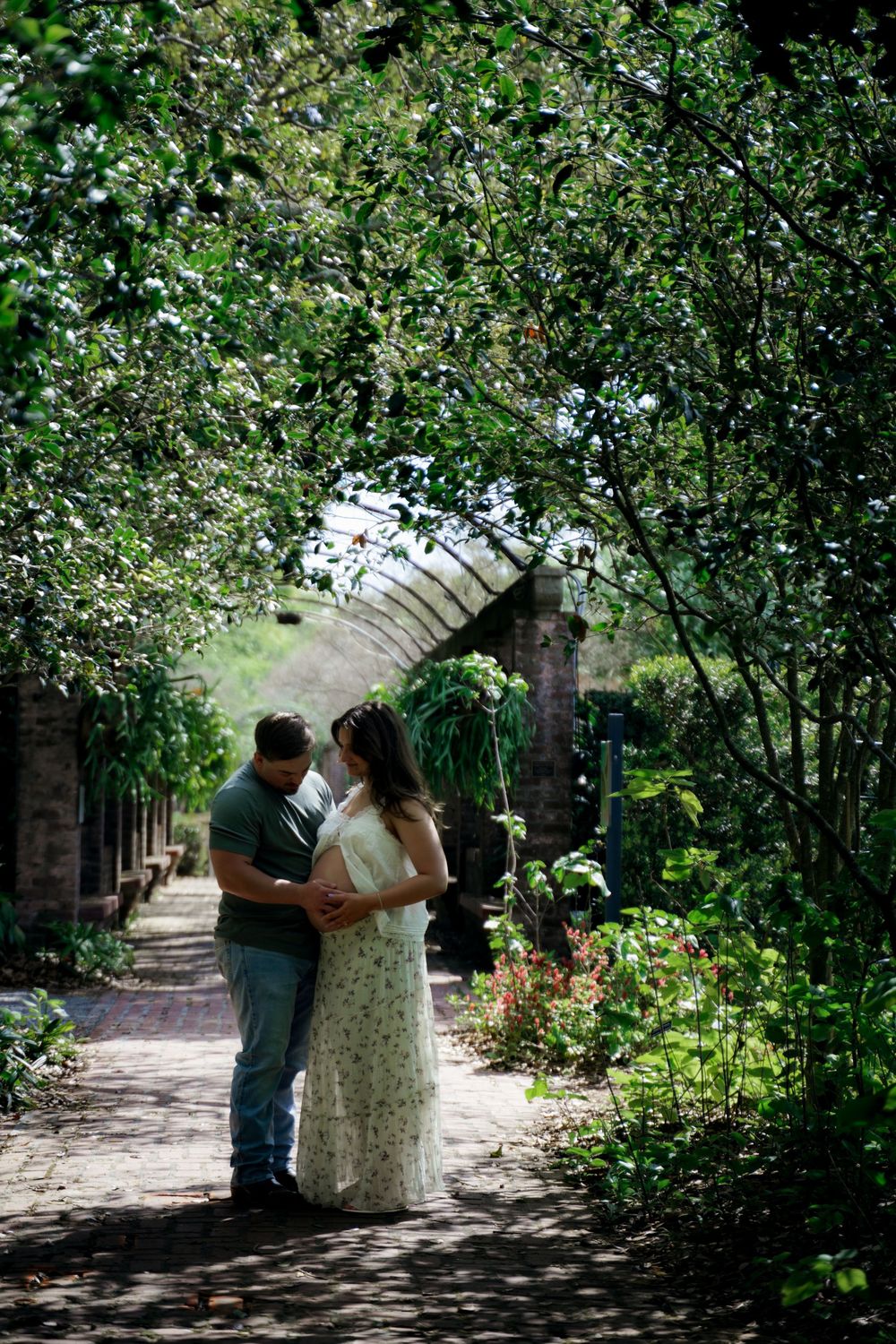 Couple sharing a romantic moment under a green arched garden tunnel with colorful flowers.