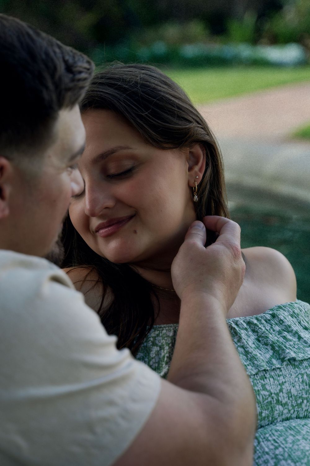 Couple sharing a tender romantic moment outdoors, man gently touching womans neck as she smiles with eyes closed.