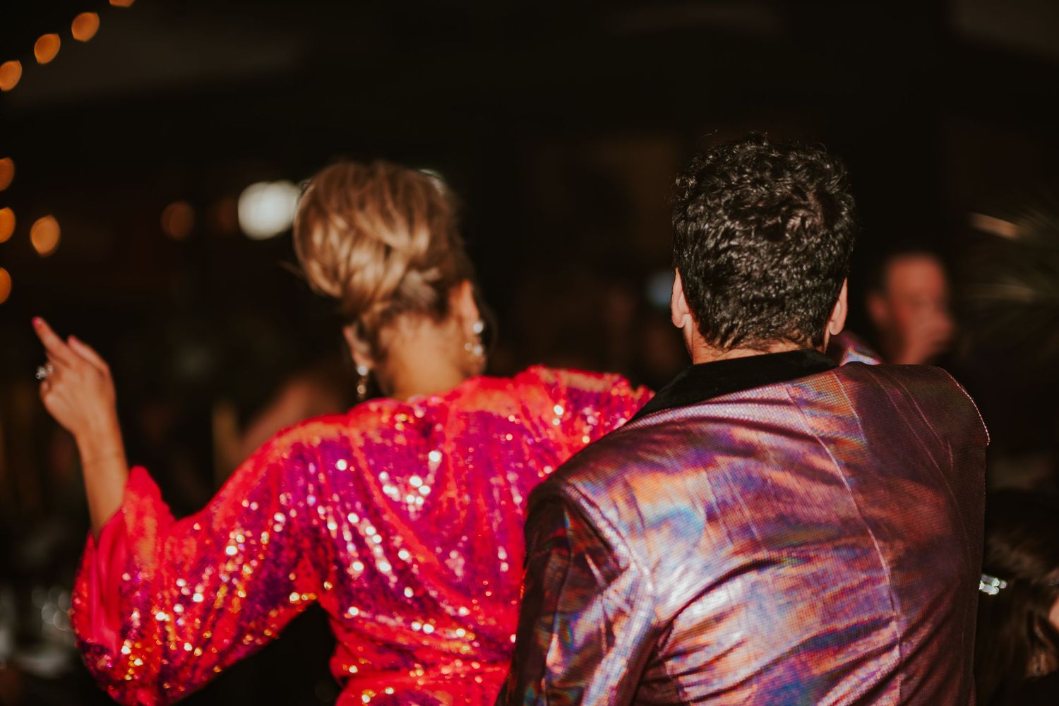 A couple dancing together at a party wearing sparkly and metallic outfits under ambient lighting.