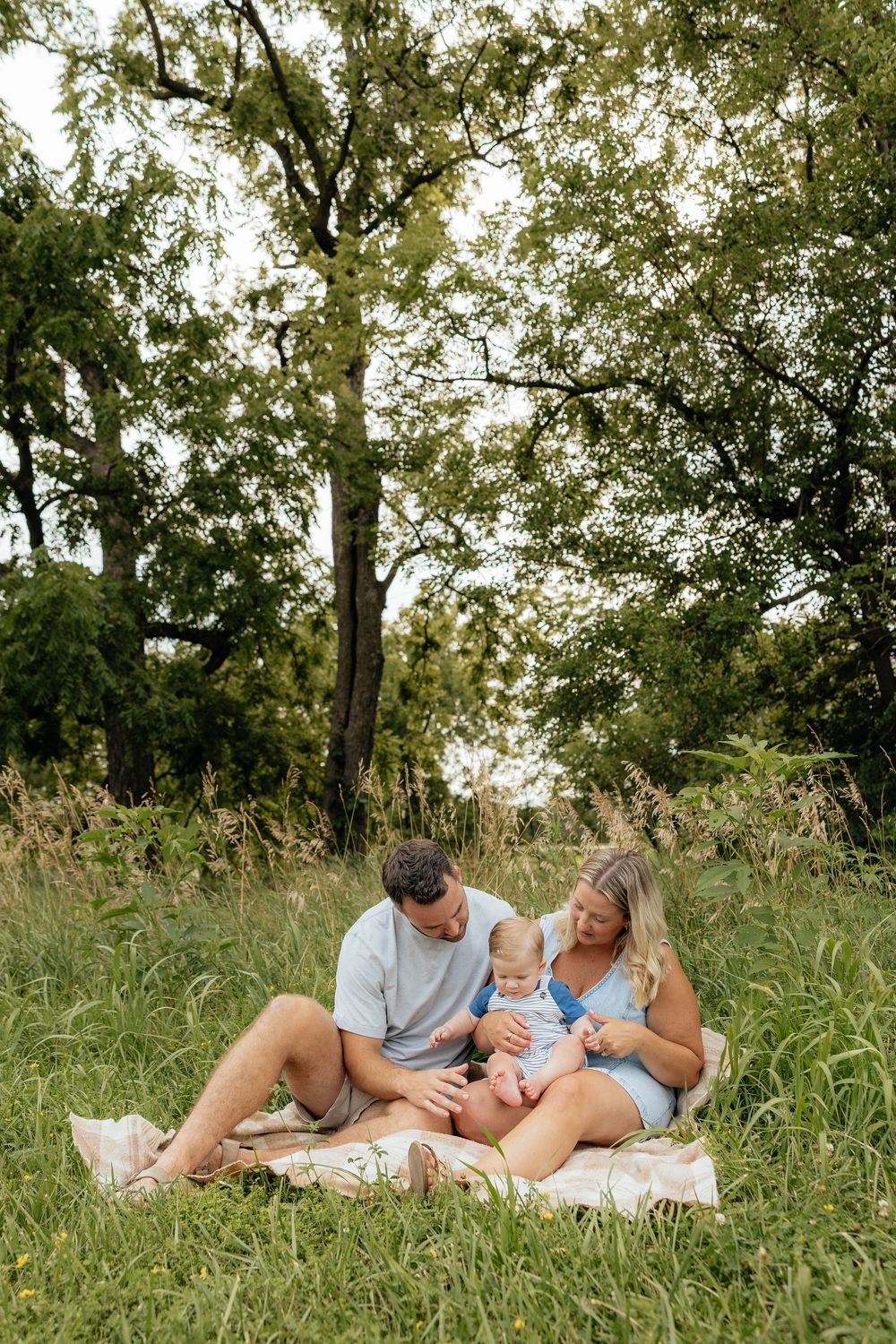 A family spends quality time together relaxing on a blanket in a grassy meadow on a sunny summer day.