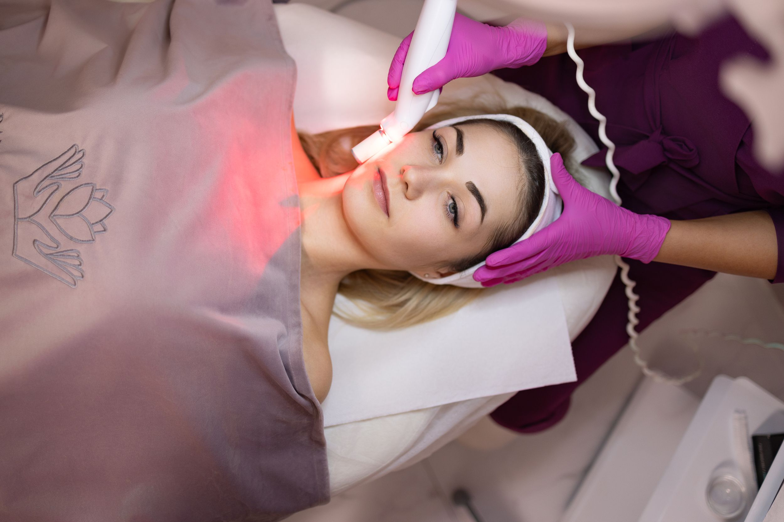 Client receives professional facial treatment with red light therapy in spa setting.