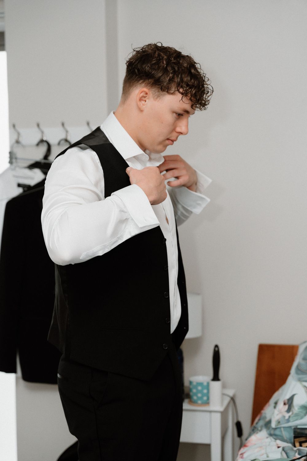 Side view of someone adjusting their tie while wearing a formal black vest and white dress shirt.