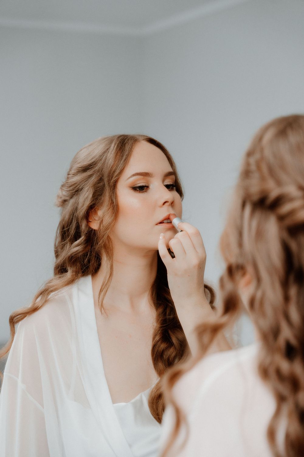Makeup artist applying lip product on a bride during wedding preparations in a light and airy setting.