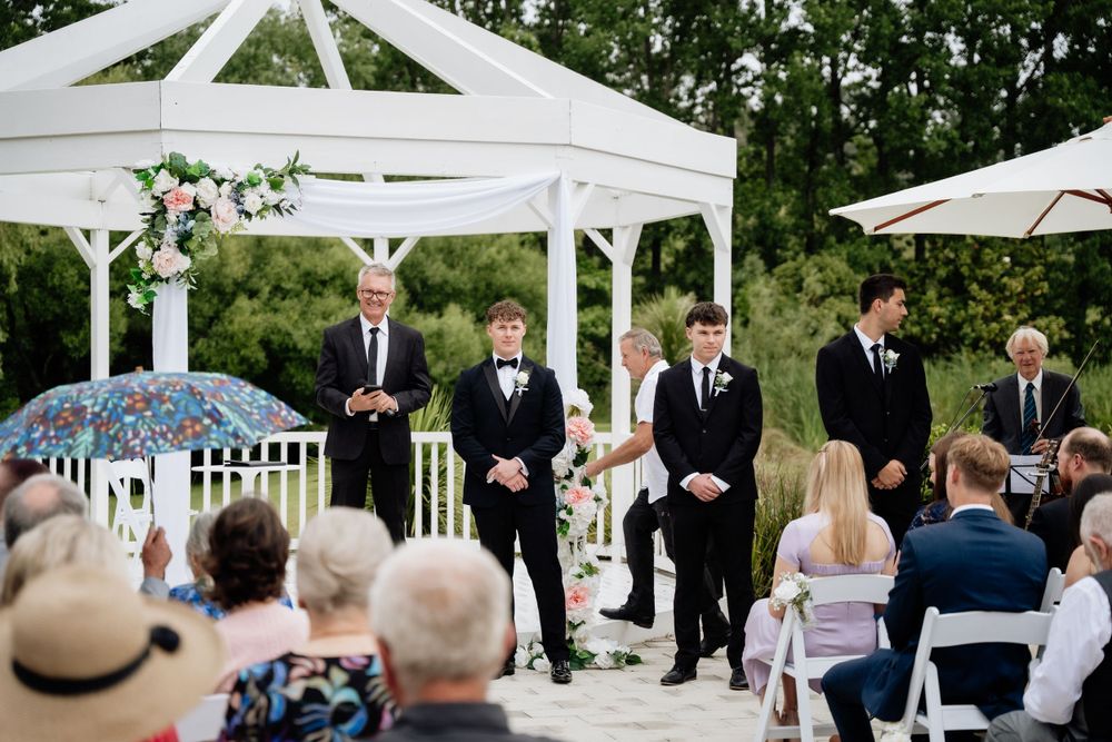Formal wedding ceremony taking place under an elegant white gazebo with guests seated outdoors.