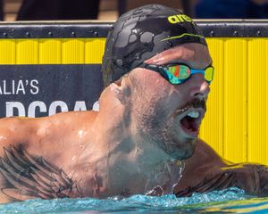 Swimmer emerges from pool wearing black swim cap and reflective goggles during competition.