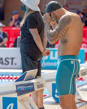 Two figures stand at poolside discussing during swimming competition event.
