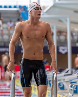 Swimmer in racing jammers grips pool rails while exiting the water after competition.