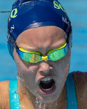 Swimmer in blue cap and mirrored goggles emerges from water during competitive race.
