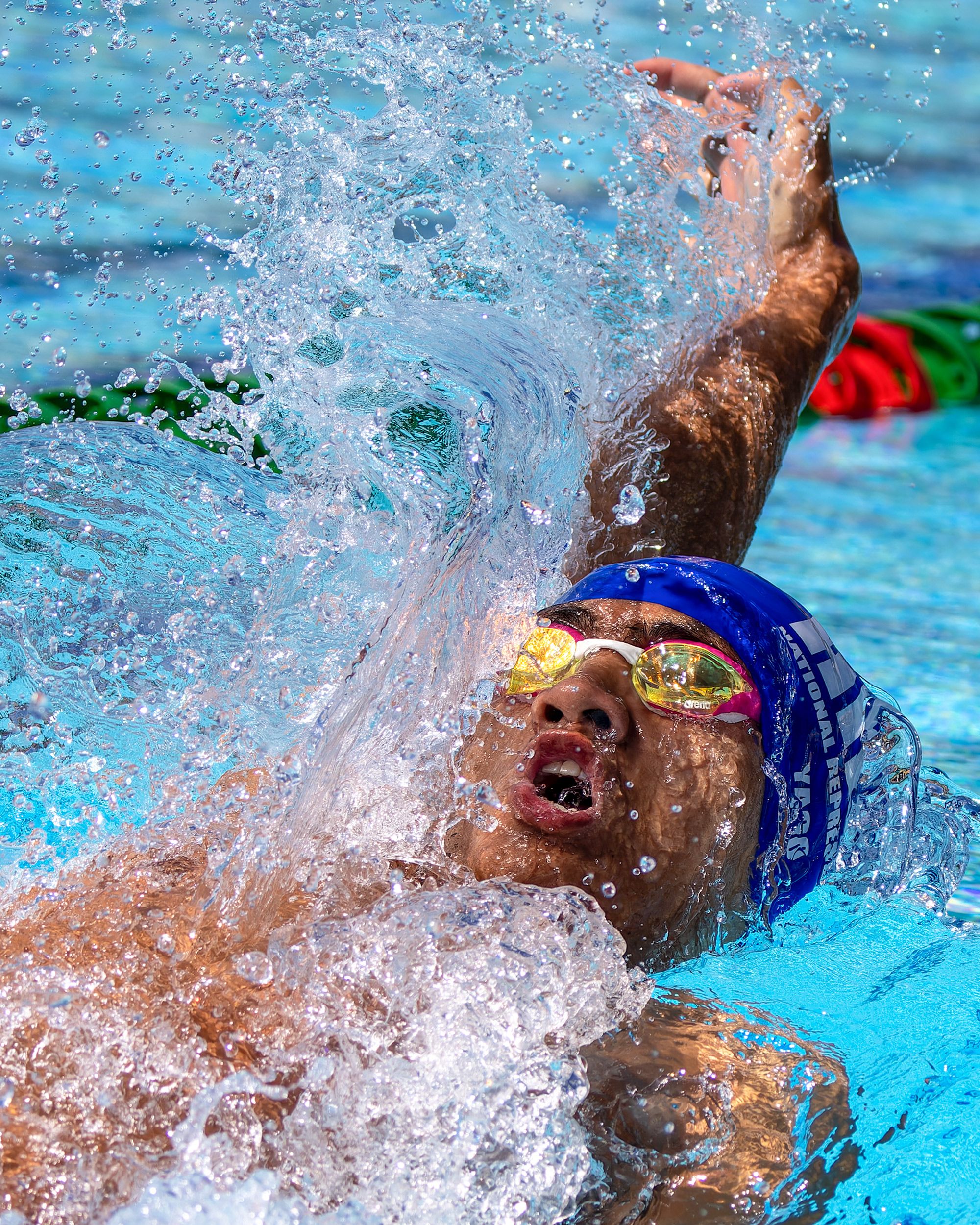 Swimmer performing backstroke with water splashing during competition.