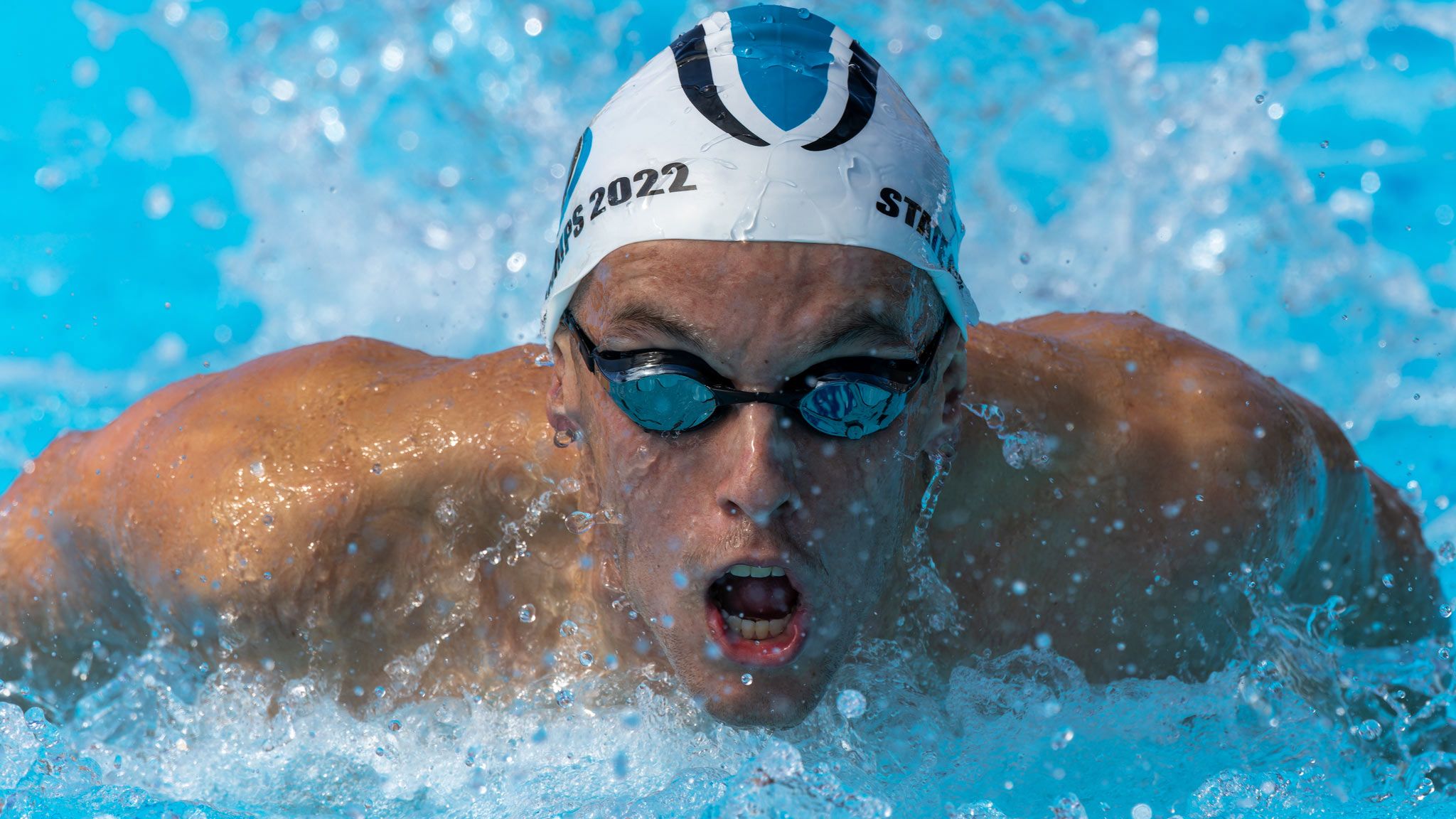 Swimmer performing butterfly stroke with intense expression during competition.
