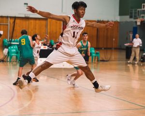 Basketball player in white jersey playing defense during indoor basketball game.