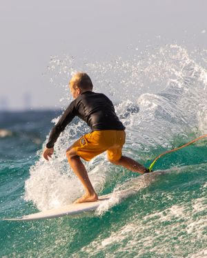 Surfer in black wetsuit and orange shorts riding ocean wave with dramatic spray.