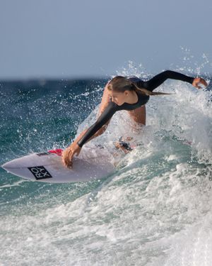 Female surfer performing dramatic turn on white wave crest with ocean spray.