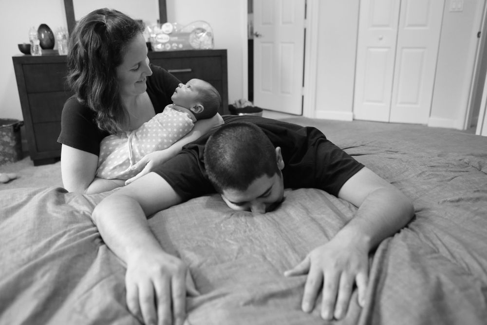 Black and white intimate family moment captured on bed with sleeping infant.