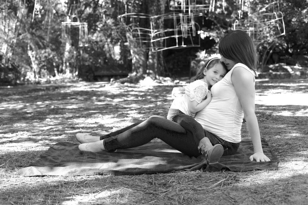 Black and white photo of pregnant woman sitting outdoors with child in natural setting.