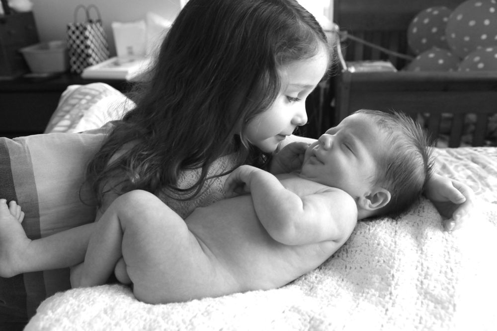 A tender black and white portrait showing a parent and baby sharing an intimate moment on a bed.