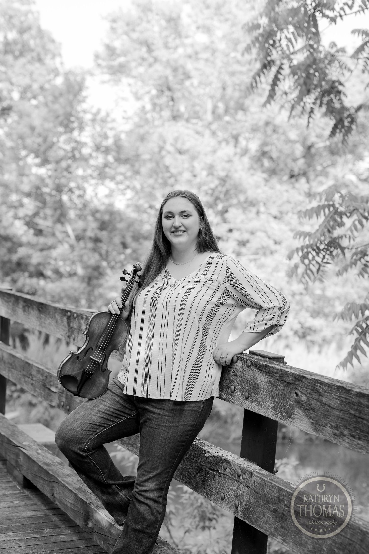 Black and white portrait of musician with violin on wooden bridge.