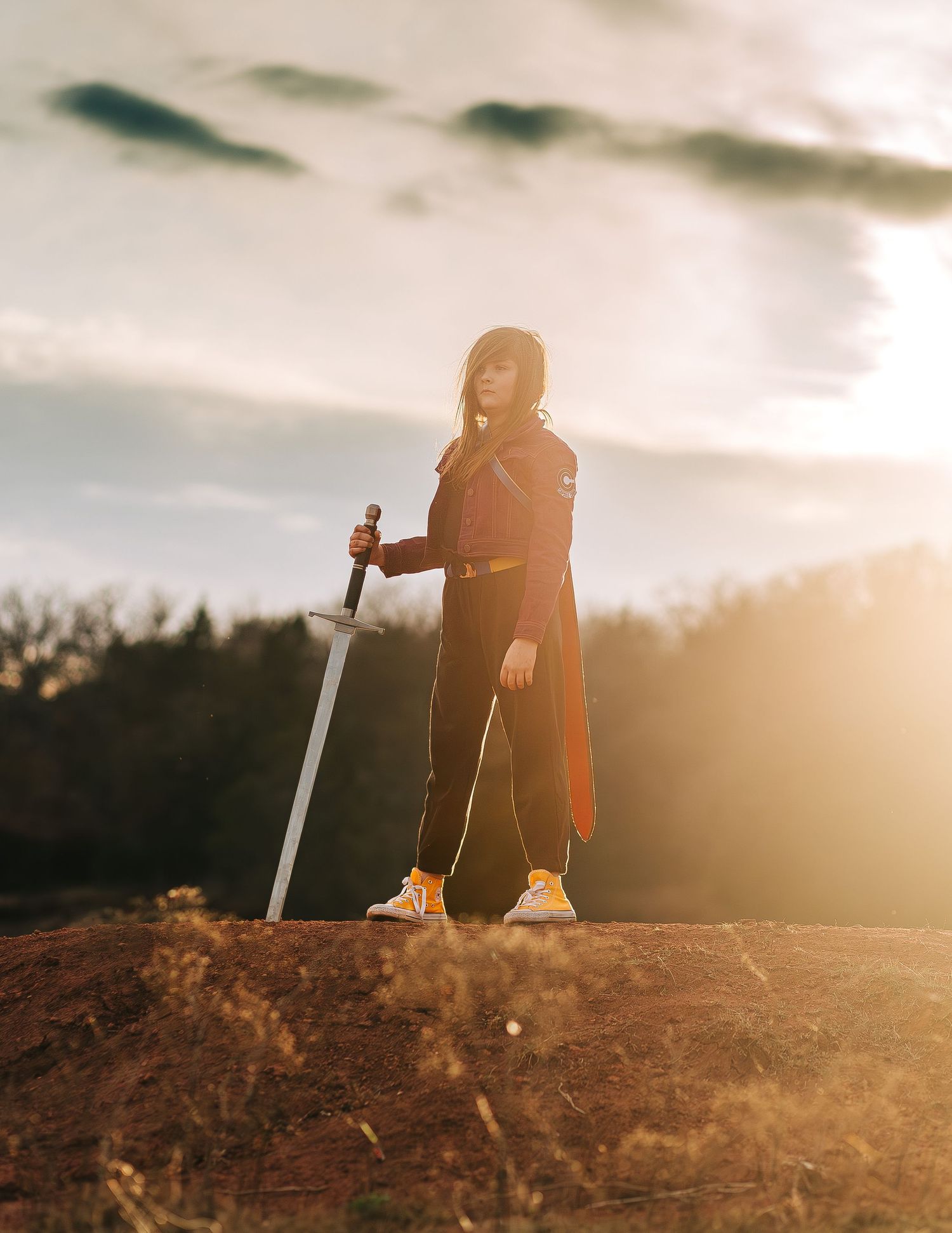 Silhouette of person holding sword at sunset on hill with dramatic lighting.