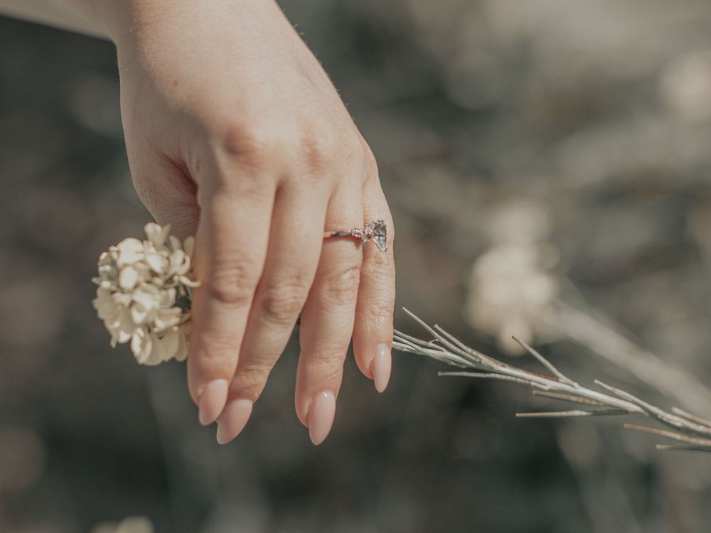 Close up of engagement ring on hand holding dried flower stem.