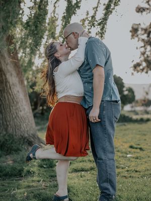 Playful engagement photo of couple kissing under tree branches.