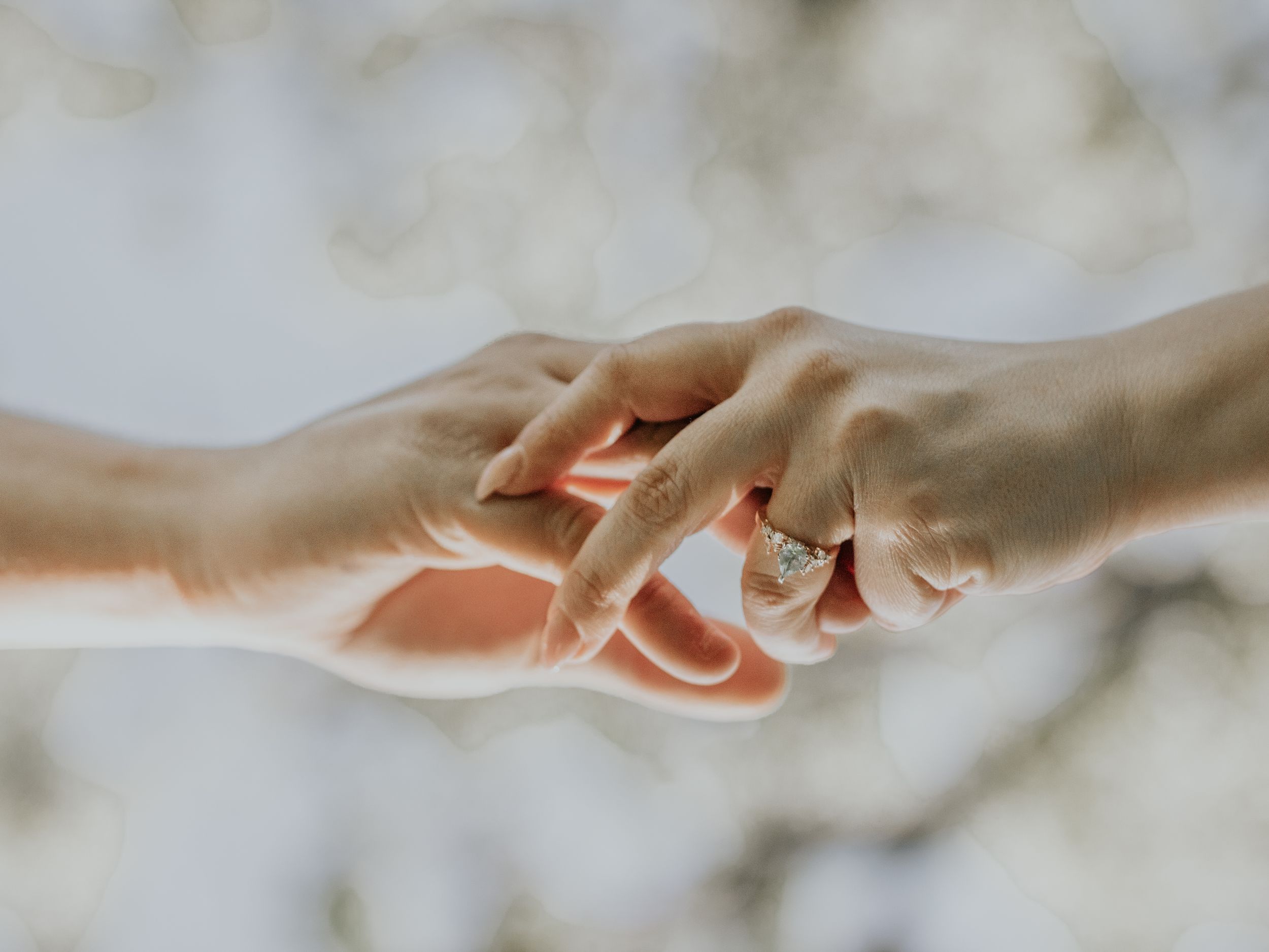 Artistic close-up photo of two hands gently touching against blurred background.