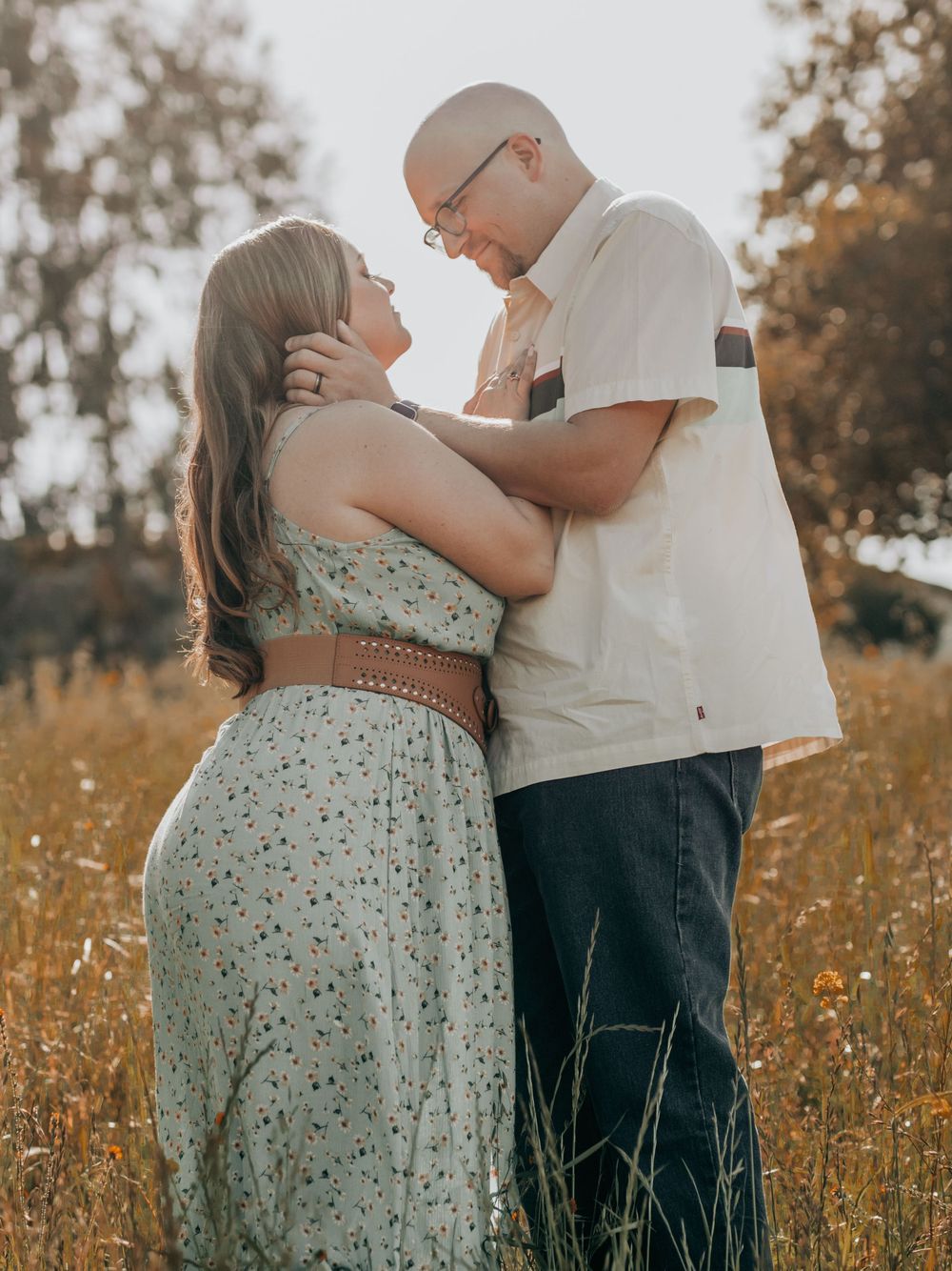 Romantic couple embracing in golden field during sunset engagement photoshoot.