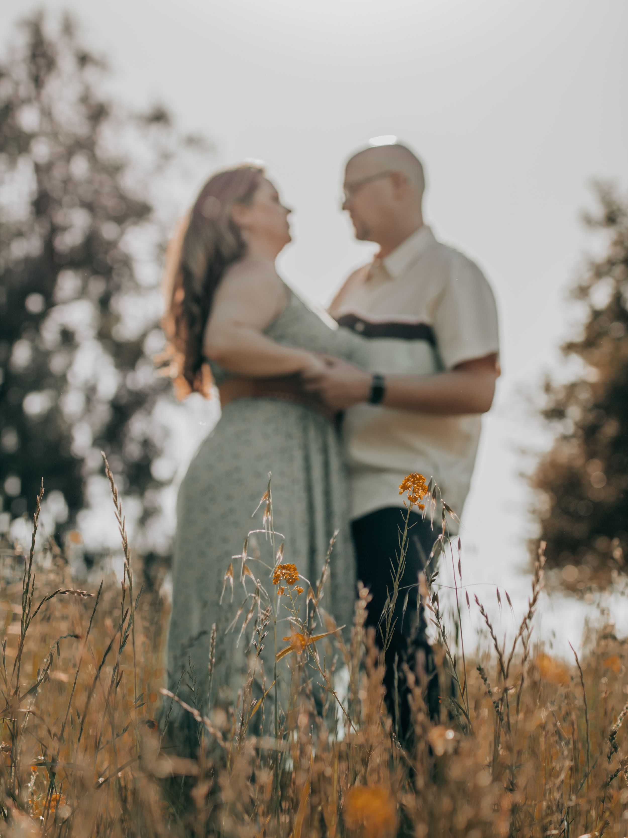 Couple standing together in tall grass field during golden hour photoshoot.