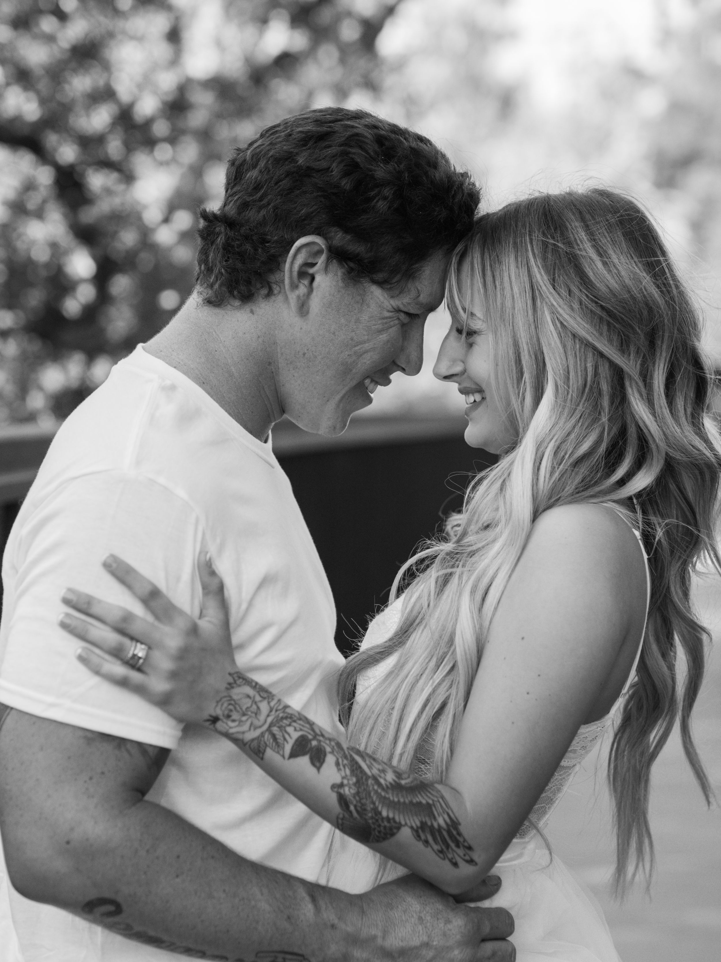 An intimate black and white portrait of a couple sharing a tender moment outdoors.