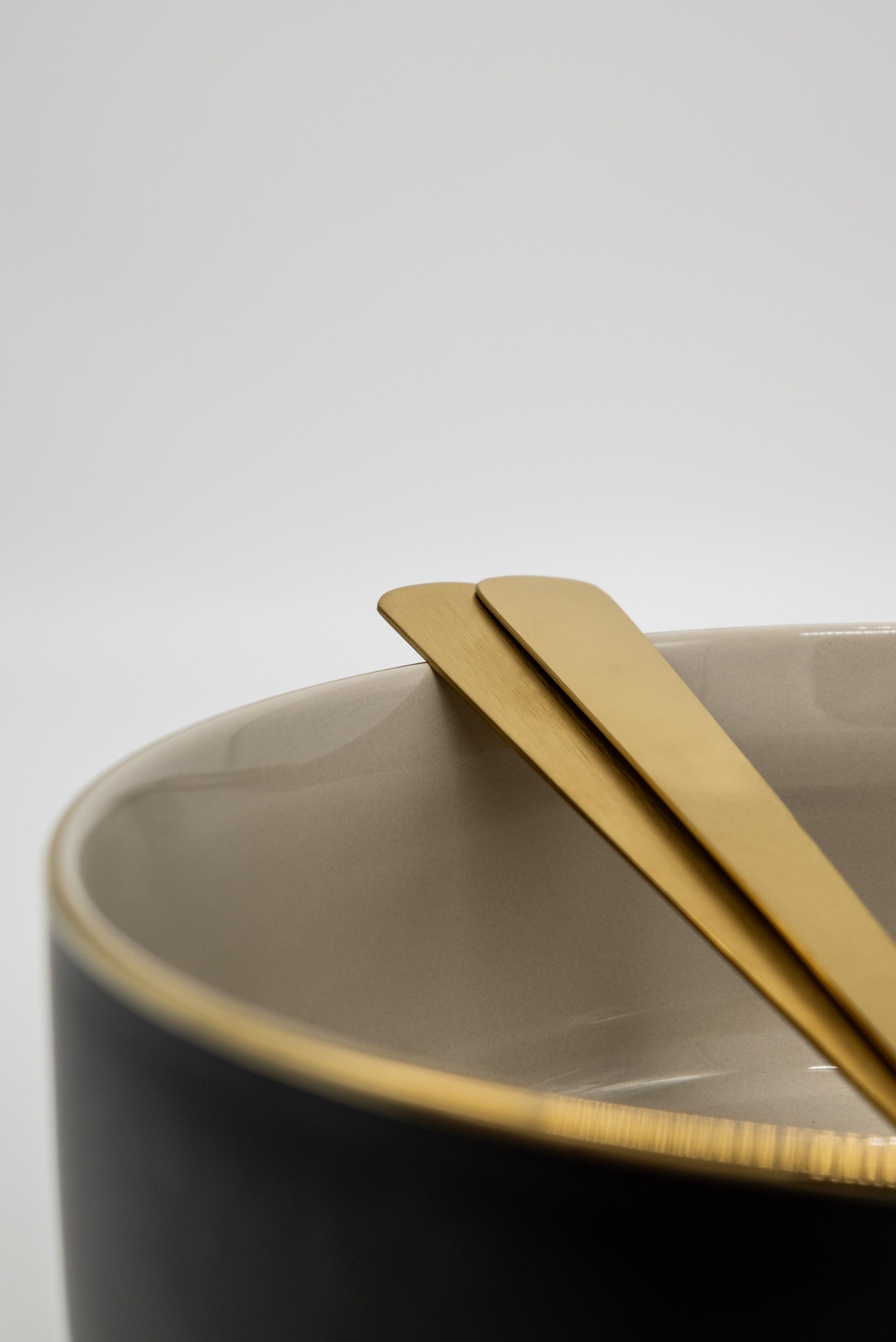 Minimalist place setting with gold utensils on a black and white ceramic bowl.