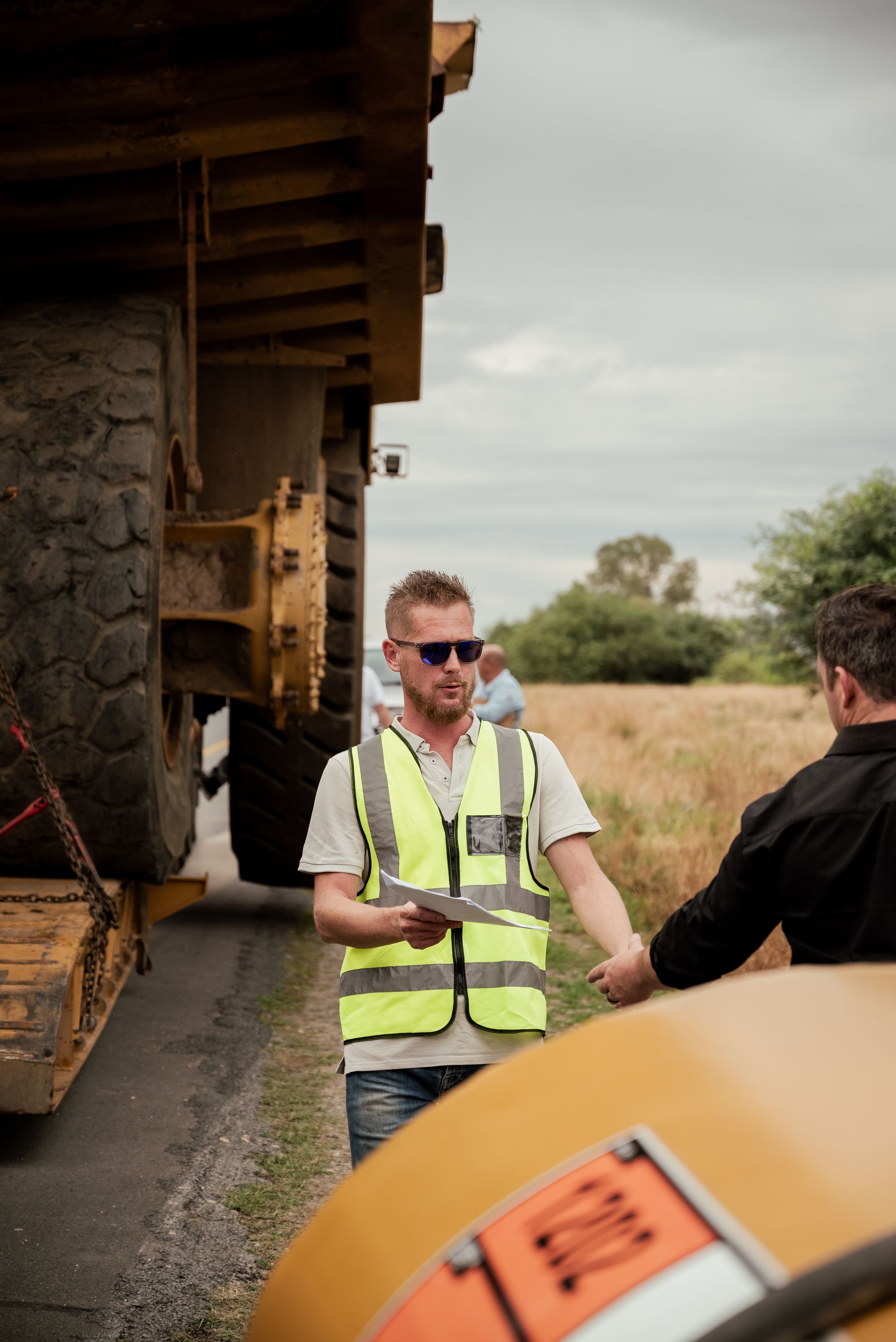 A worker in a high-visibility vest discusses details near an industrial loading area.