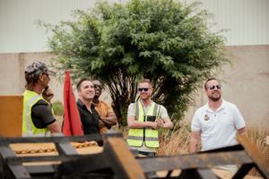 Workers in safety vests gather around equipment for an outdoor meeting.