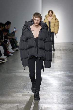 Models walk the runway showcasing oversized black and yellow puffer jackets during a contemporary fashion show.