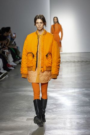 Orange quilted jacket and matching pants ensemble on fashion runway.