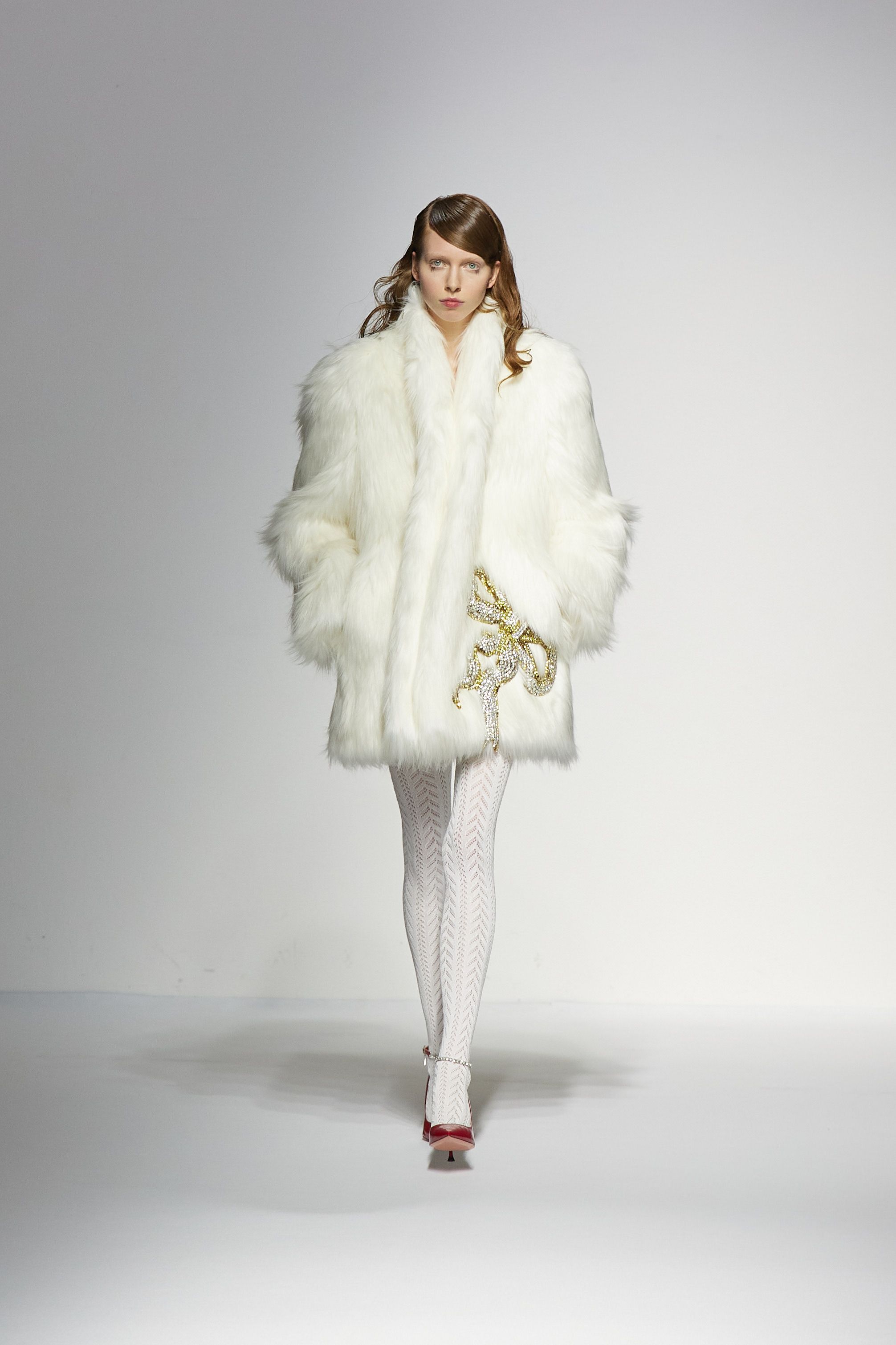Luxurious white fur coat styled with white tights on fashion runway.