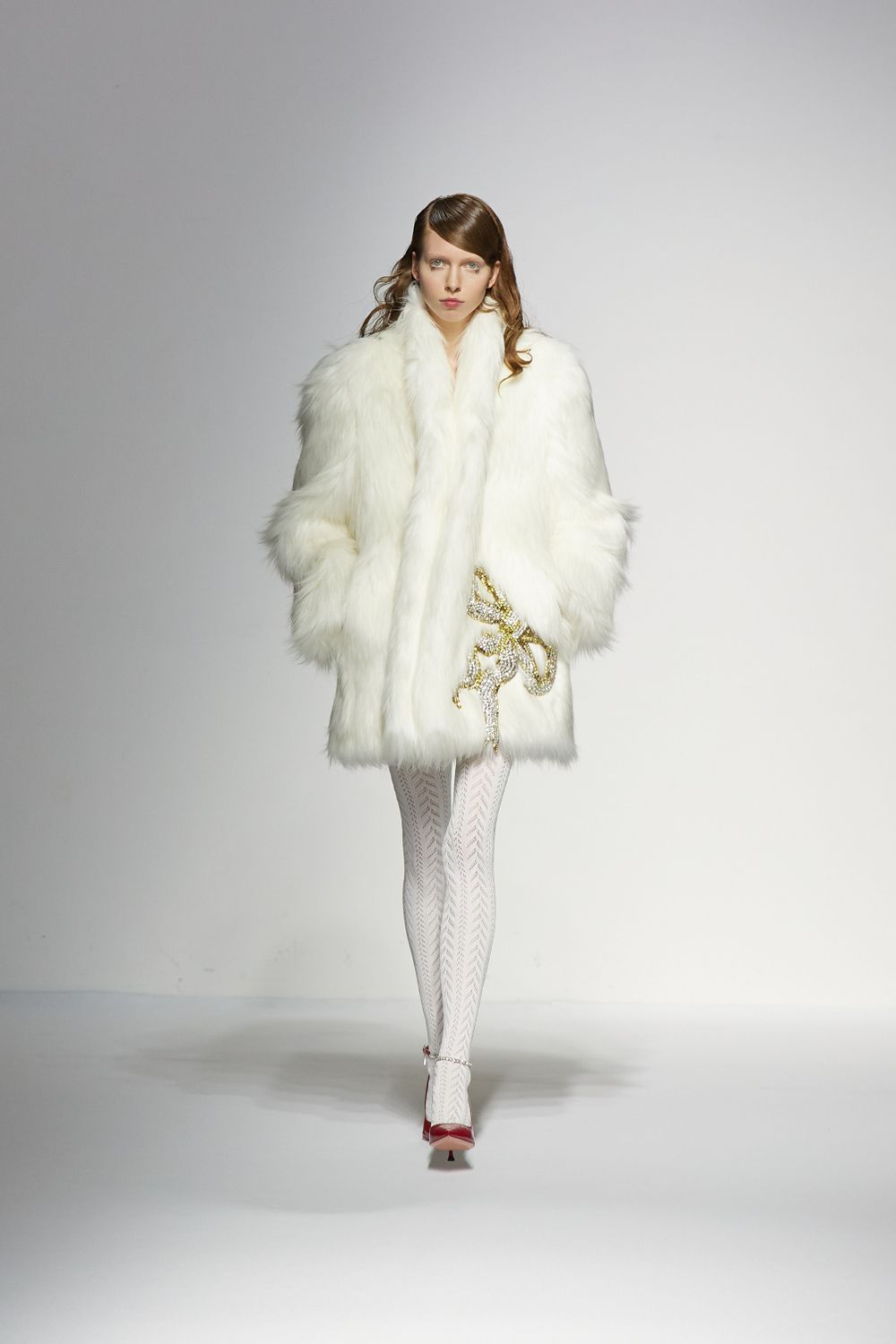 Luxurious white fur coat styled with white tights on fashion runway.
