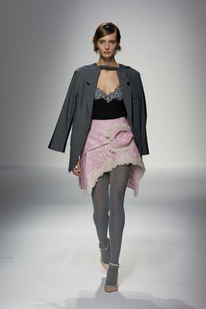 Grey blazer and pink asymmetrical skirt combination on fashion runway.