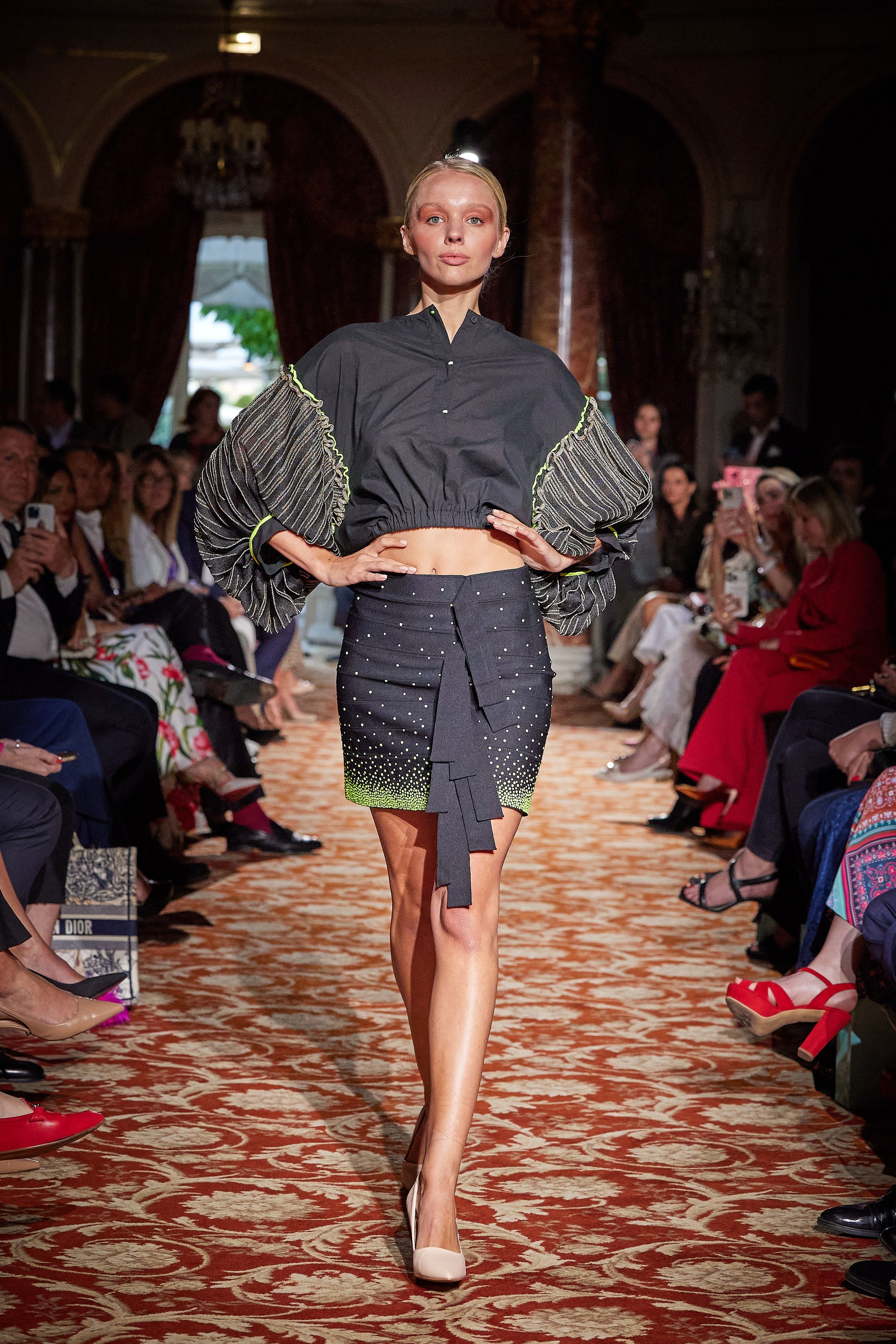 Fashion model walking runway in avant-garde gray outfit with structured sleeves and short skirt.