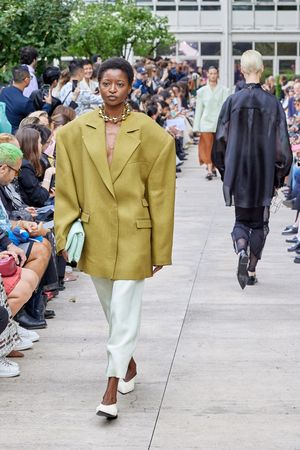 Oversized mustard blazer paired with mint pants on fashion runway with seated audience.