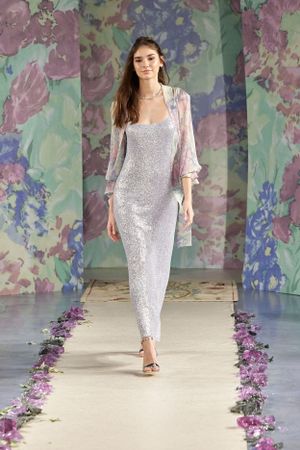 Shimmering white sequined gown with sheer sleeves on floral runway.