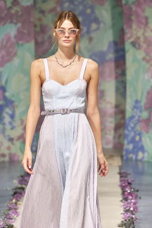 White pleated sundress with metallic belt on floral backdrop runway.