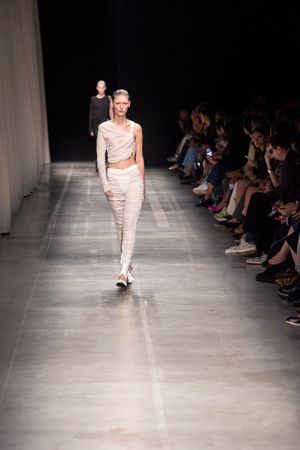 Minimalist draped white ensemble on dark runway with seated audience.