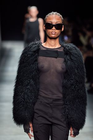 All-black ensemble featuring sheer top and dramatic furry coat on fashion runway.