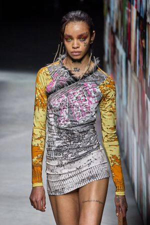 Avant-garde mini dress with mixed prints and metallic details on dark runway.
