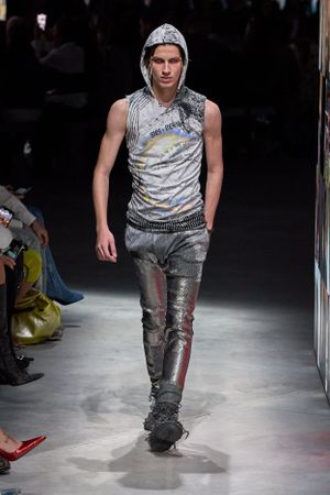 Metallic hooded vest with distressed pants on dark runway.