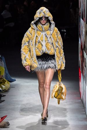 Yellow puffy winter coat with silver accents styled with a fluffy skirt and matching handbag on fashion runway.