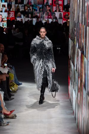 Dramatic gray feathered coat ensemble shown on runway with dark urban backdrop.