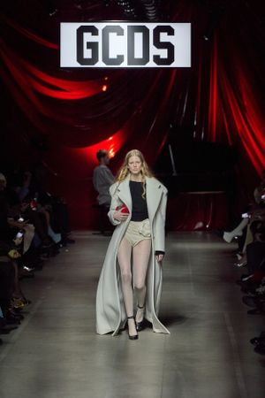 Long beige coat paired with shorts at GCDS fashion show with red lighting effects.