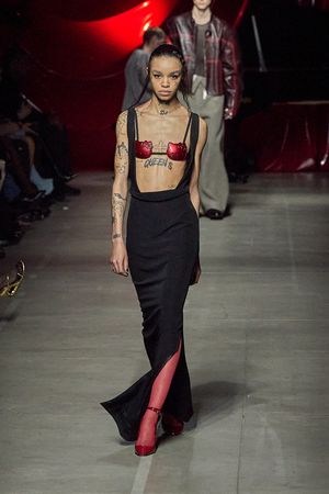 Black maxi skirt paired with red bra top and boots on dimly lit runway.