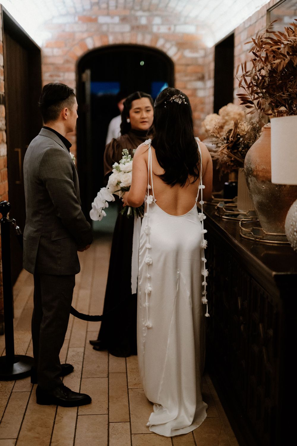 A couple at their wedding ceremony in an intimate brick-walled venue with backlit archway and rustic decor.